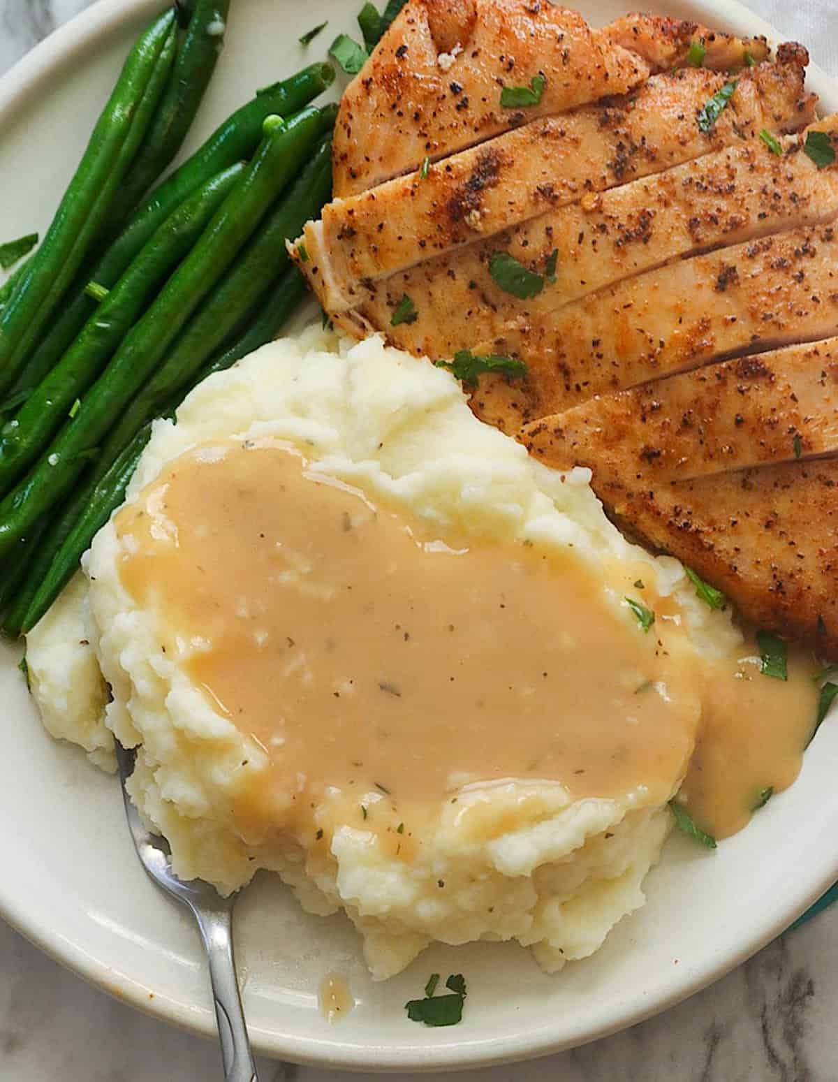 Enjoying chicken and mashed potatoes smothered in gravy wit roasted green beans on the side