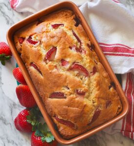 Insanely delicious freshly baked strawberry bread ready to slice with fresh strawberries on the side