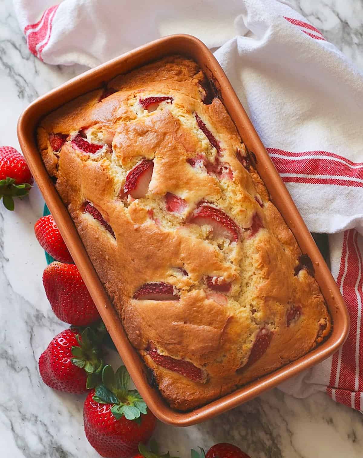 Insanely delicious freshly baked strawberry bread ready to slice with fresh strawberries on the side