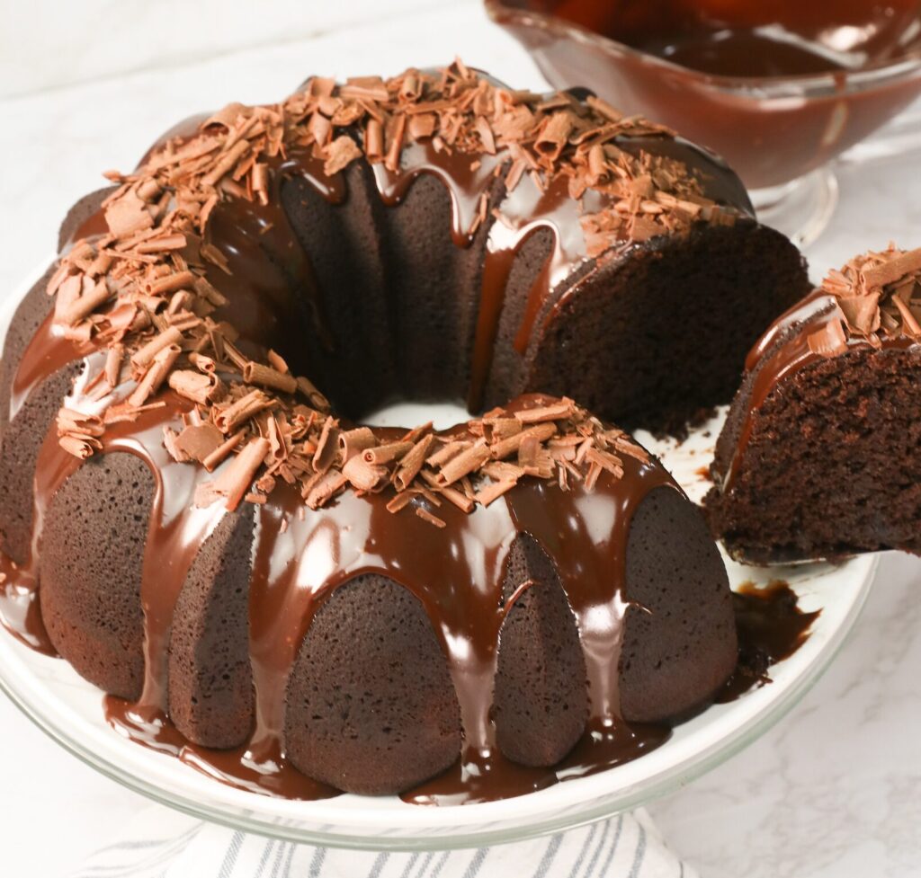 Slicing into an insanely decadent chocolate bundt cake with chocolate ganache drizzled over it and sprinkled with chocolate shavings
