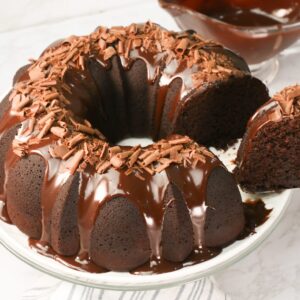 Slicing into an insanely decadent chocolate bundt cake with chocolate ganache drizzled over it and sprinkled with chocolate shavings