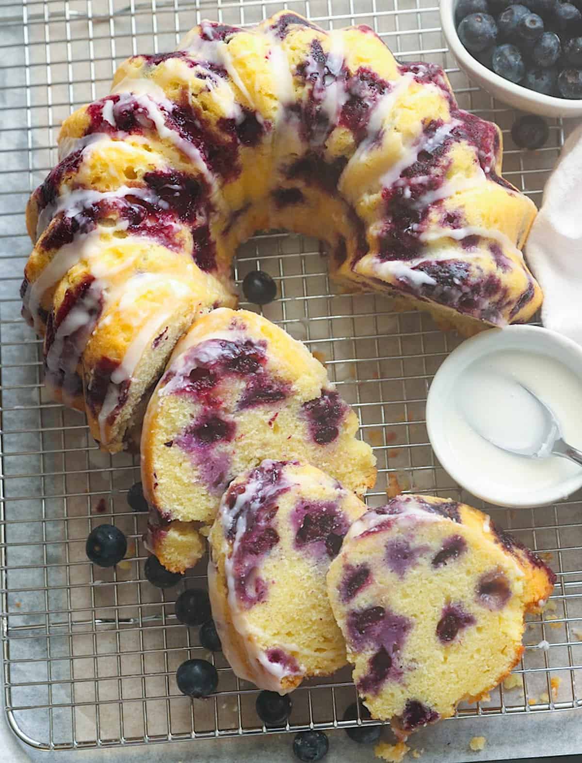 A decadent slice of blueberry bundt cake with a generous drizzle of lemon glaze on the sides