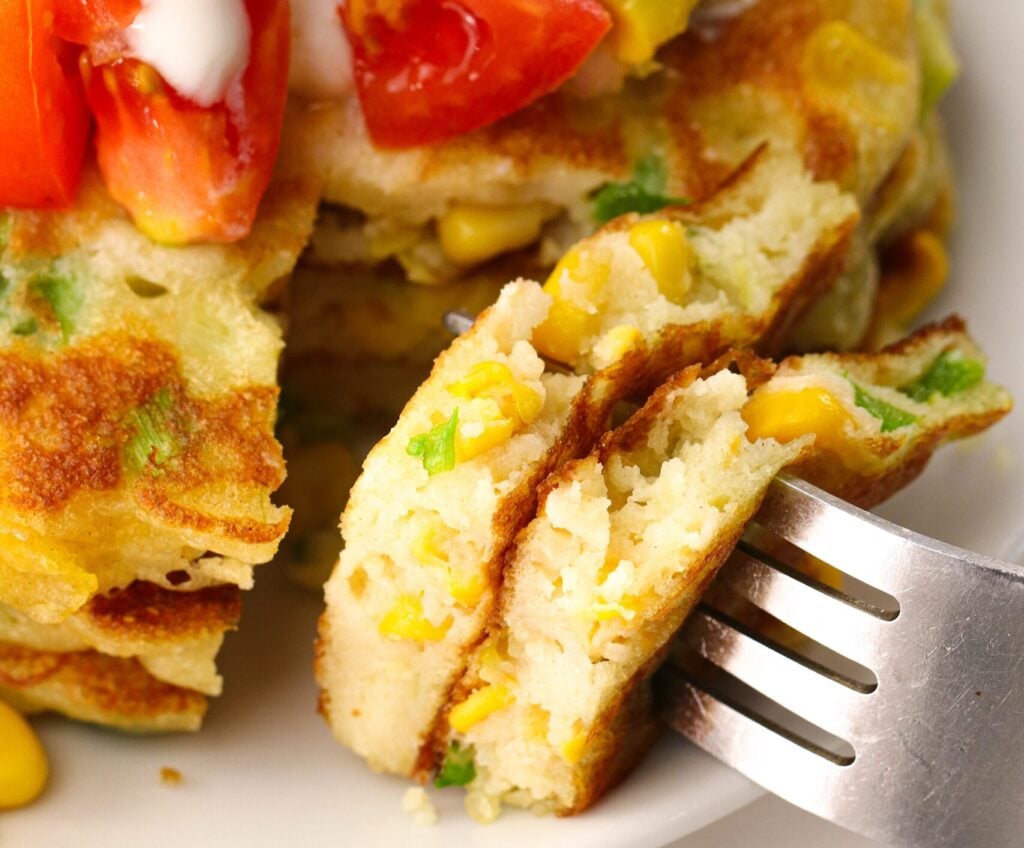 Taking a delicious bite out of a stack of corn cakes topped with sour cream, tomatoes, corn, and avocadoes