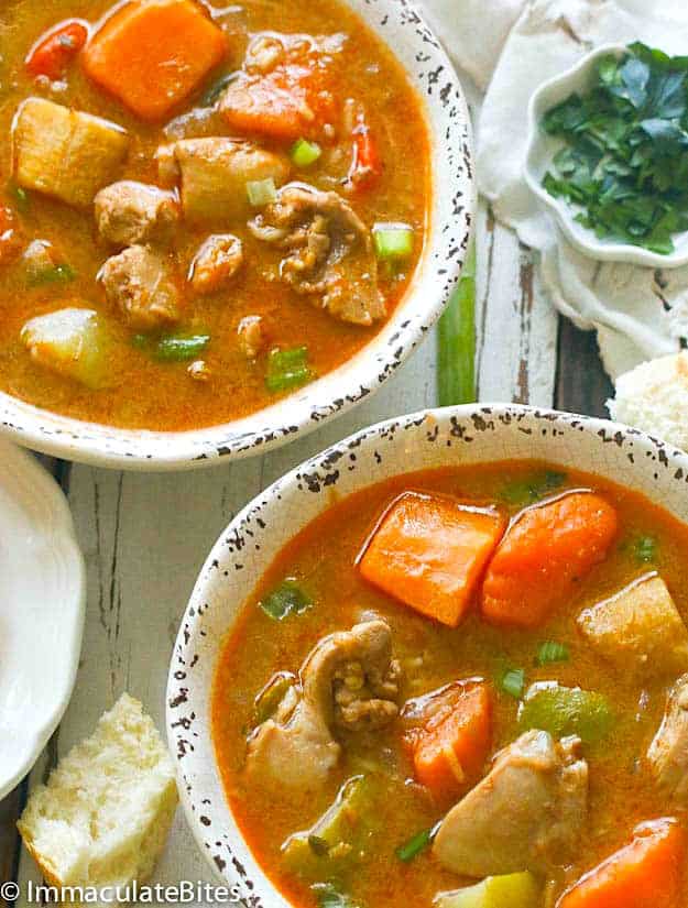 Two bowls of Jamaican Chicken and Pumpkin Soup ready to enjoy with fresh bread