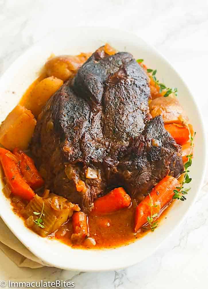 Pot roast made in a slow cooker served on a white plate with tasty carrots and potatoes