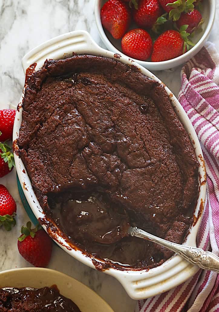 In the background is a bowl of melted chocolate cobbler garnished with fresh strawberries