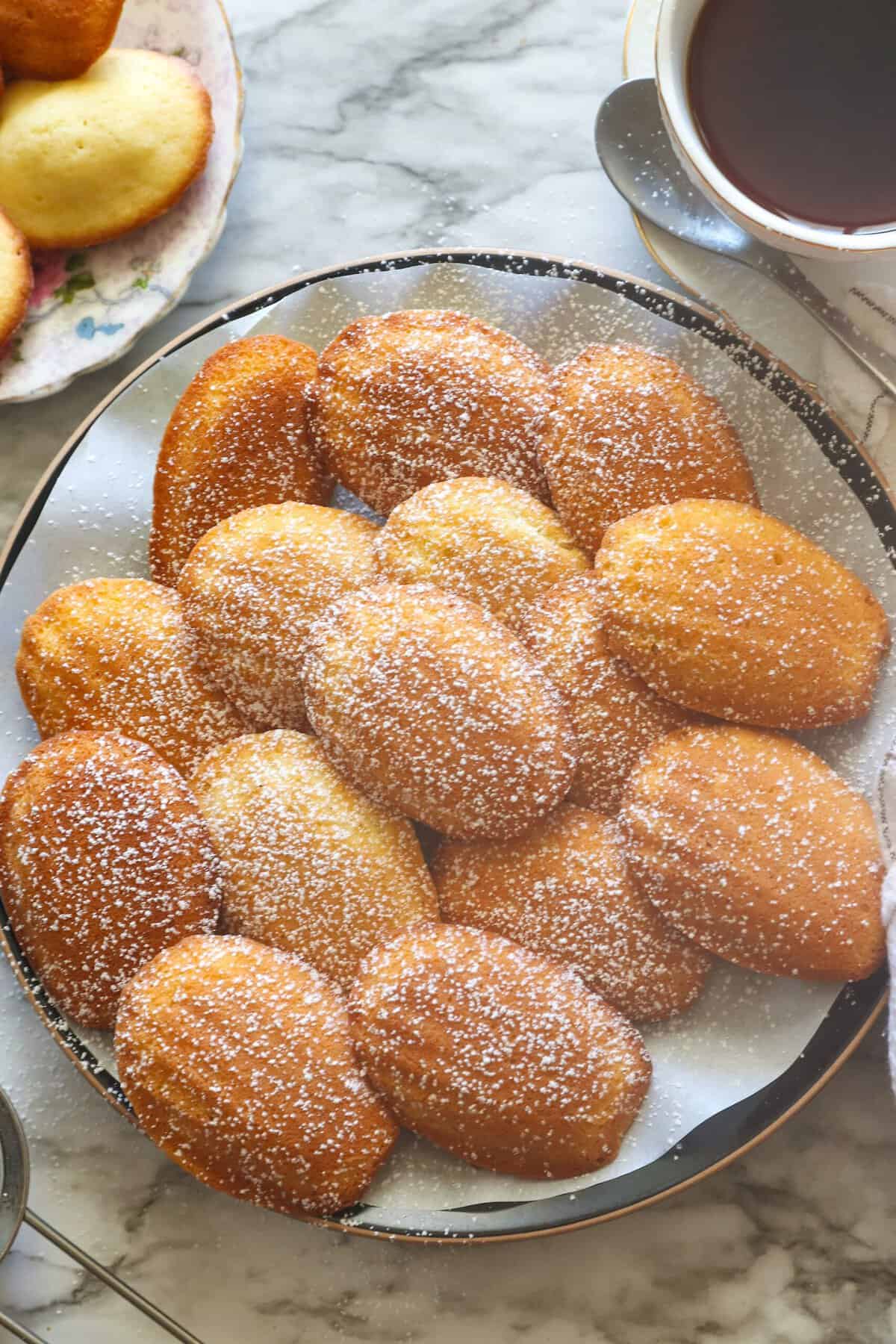 Freshly baked Madeleine cookies are dusted with powdered sugar and served immediately.