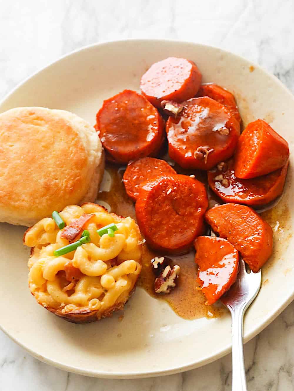 Candied yams and freshly baked biscuits adorn the plate, accompanied by bites of macaroni and cheese.