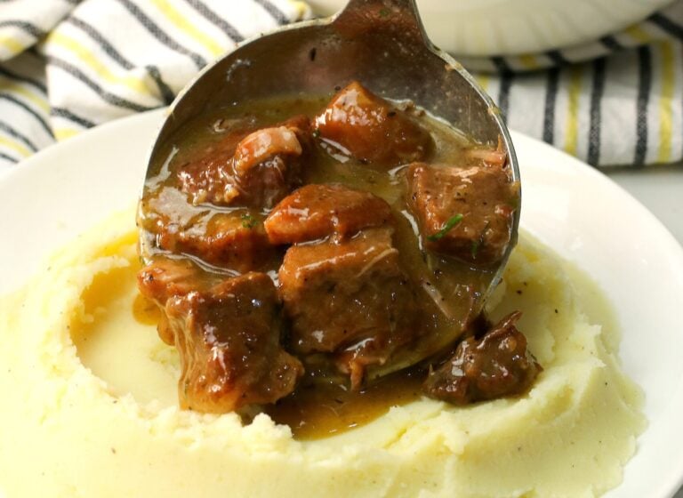 Serving fork-tender slow cooker beef tips over creamy mashed potatoes
