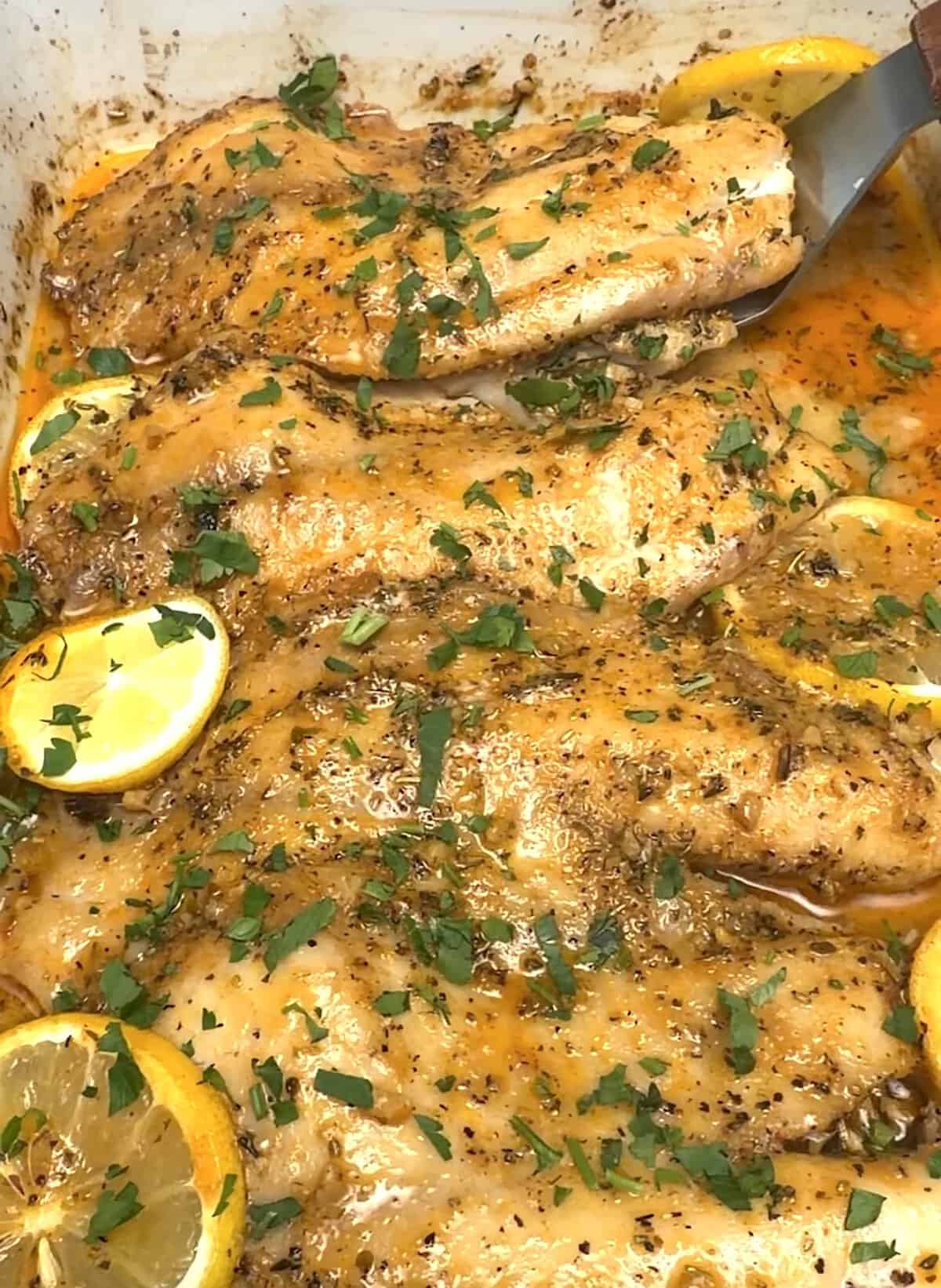 Flaky baked tilapia fresh from the oven, then garnished with lemon slices and parsley.