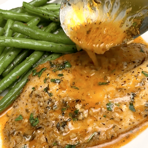 Drizzling the savory sauce over freshly baked tilapia.
