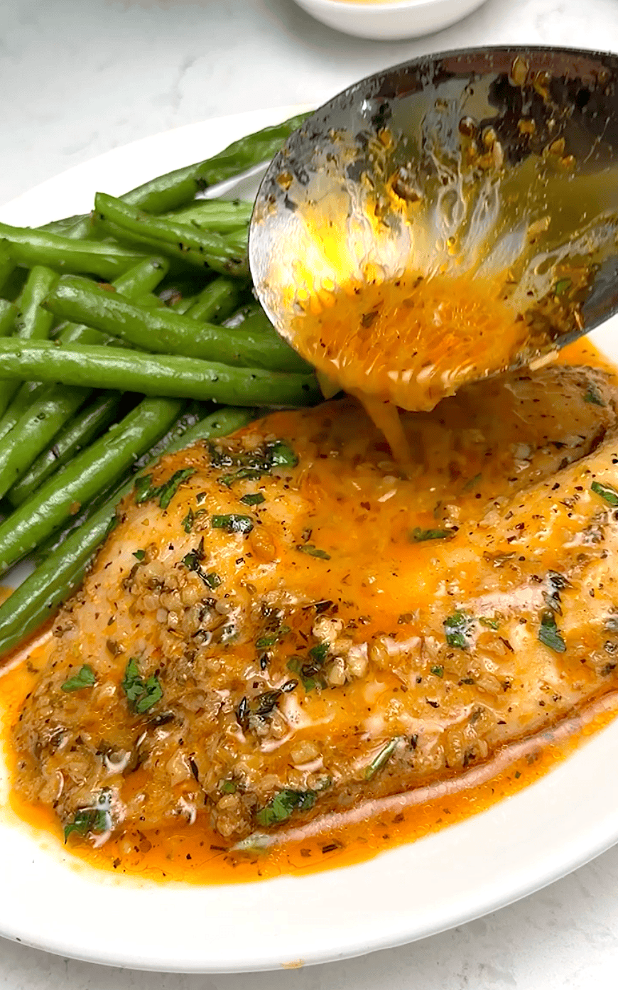 Drizzling the savory sauce over freshly baked tilapia.