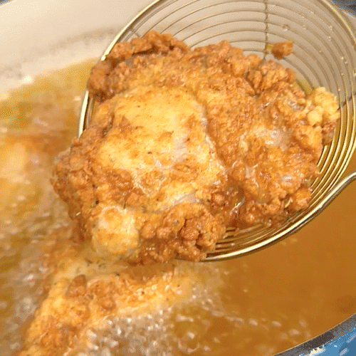 Carefully removing freshly fried chicken from the hot oil.