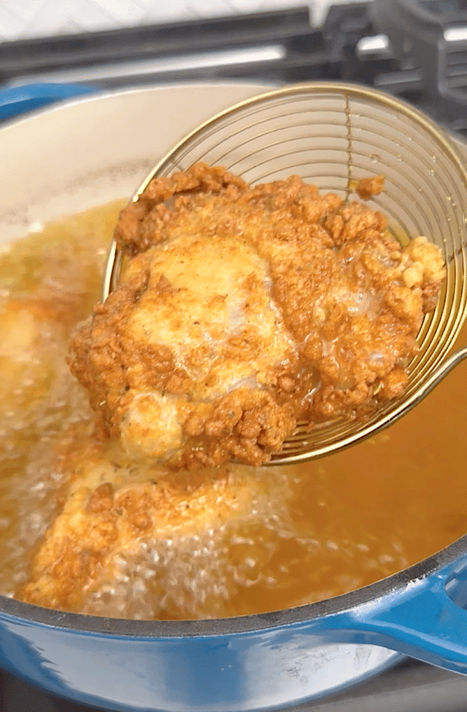 Carefully removing freshly fried chicken from the hot oil.