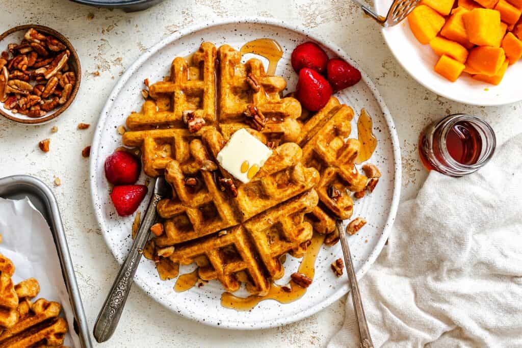 Sweet potato waffles fresh out of the waffle maker with butter, fruit, and syrup.