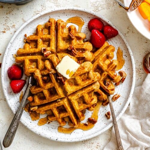 Sweet potato waffles fresh out of the waffle maker with butter, fruit, and syrup.