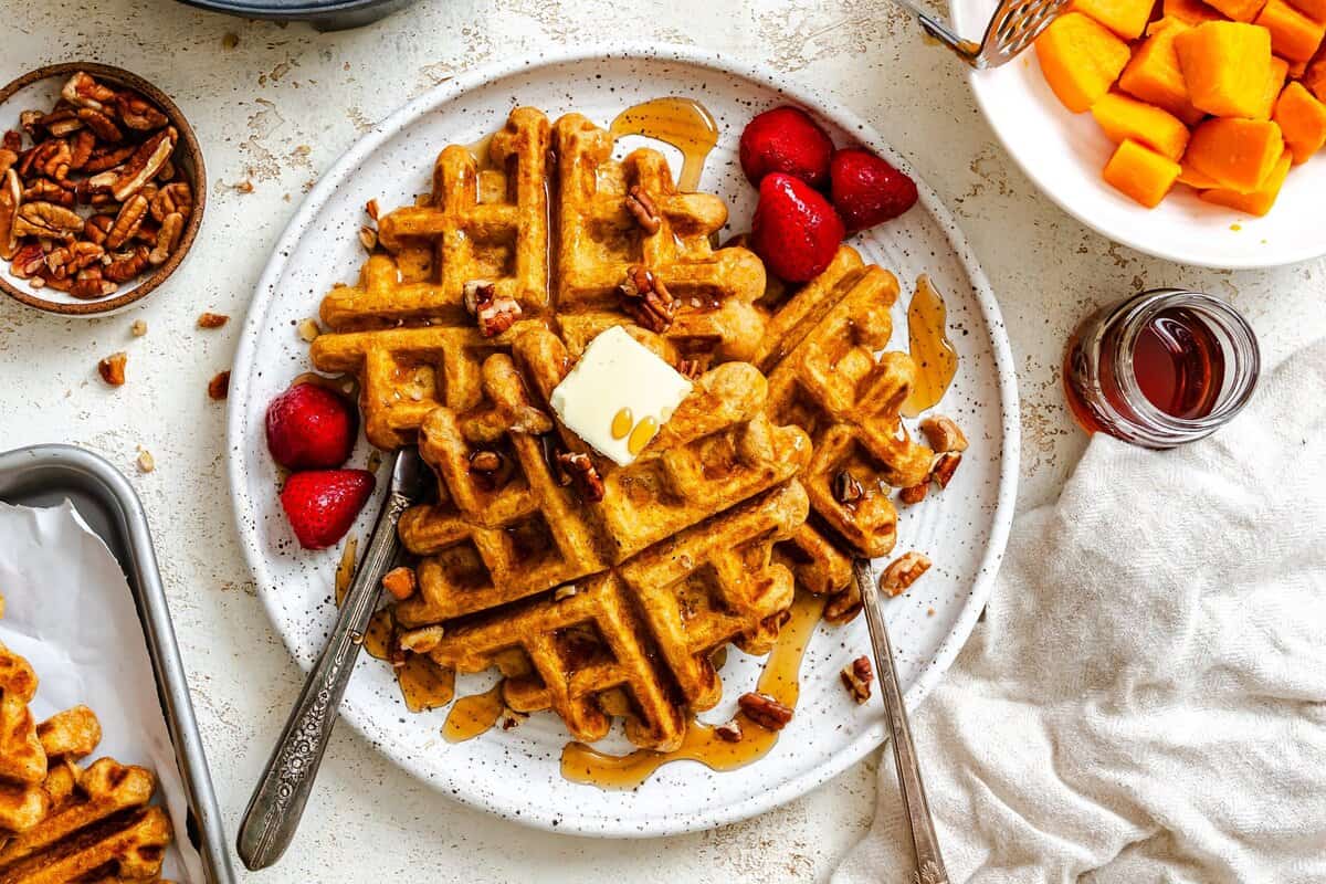 Sweet potato waffles fresh out of the waffle maker with butter, fruit, and syrup.