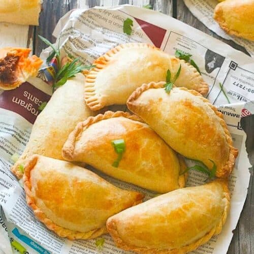 A newspaper lined basket full of freshly baked African meat pies.