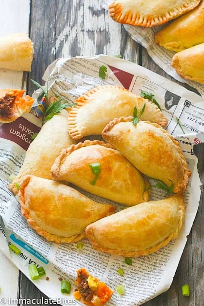 A newspaper lined basket full of freshly baked African meat pies.