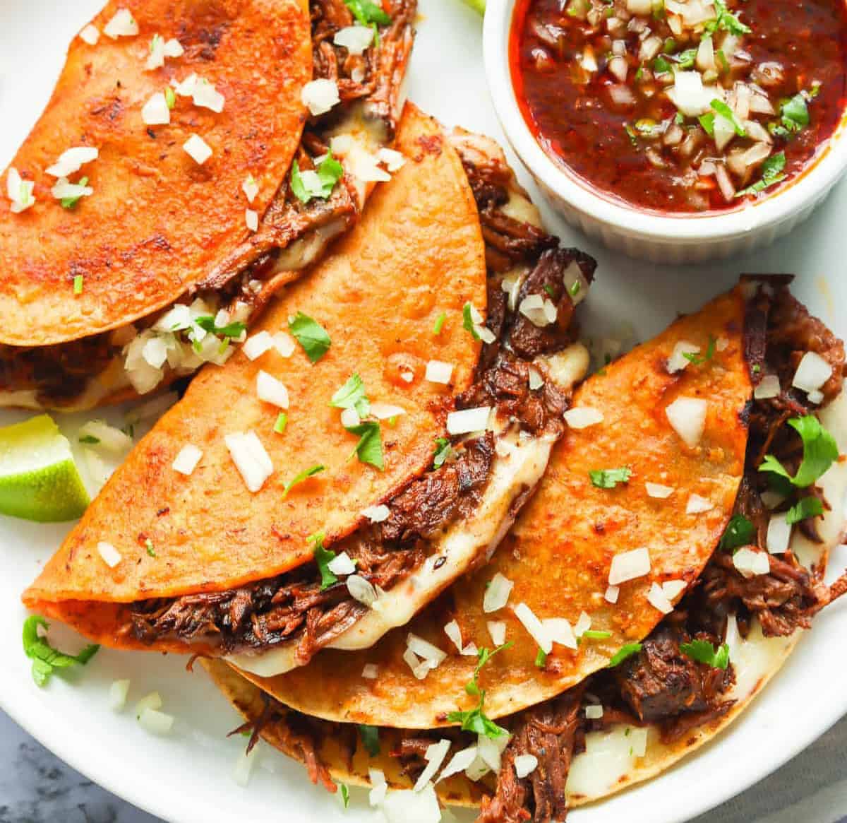 Serving up a delicious plateful of beef birria tacos with hot sauce.