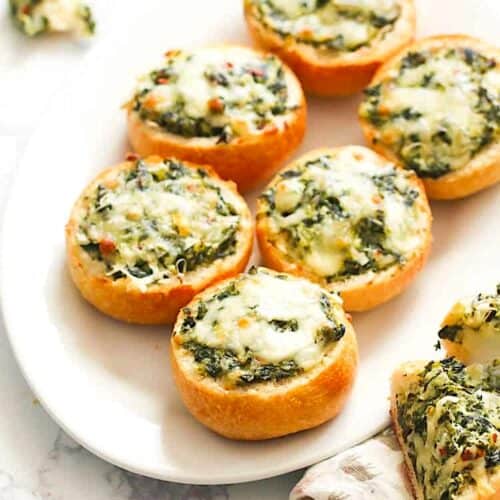 A platter full of adorable bread rolls filled with spinach dip.