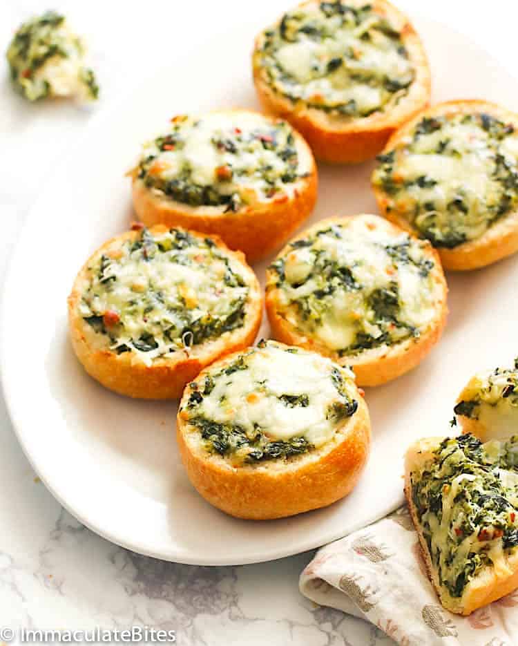 A platter full of adorable bread rolls filled with spinach dip.