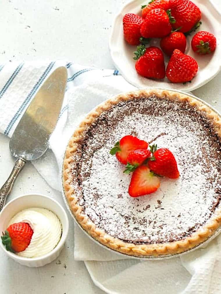 Topping homemade pie with powdered sugar, whipped cream, and fresh strawberries.
