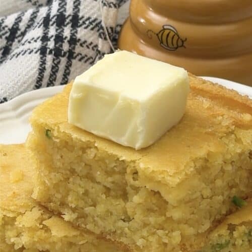Topping a stack of skillet cornbread with butter for a great bread side.