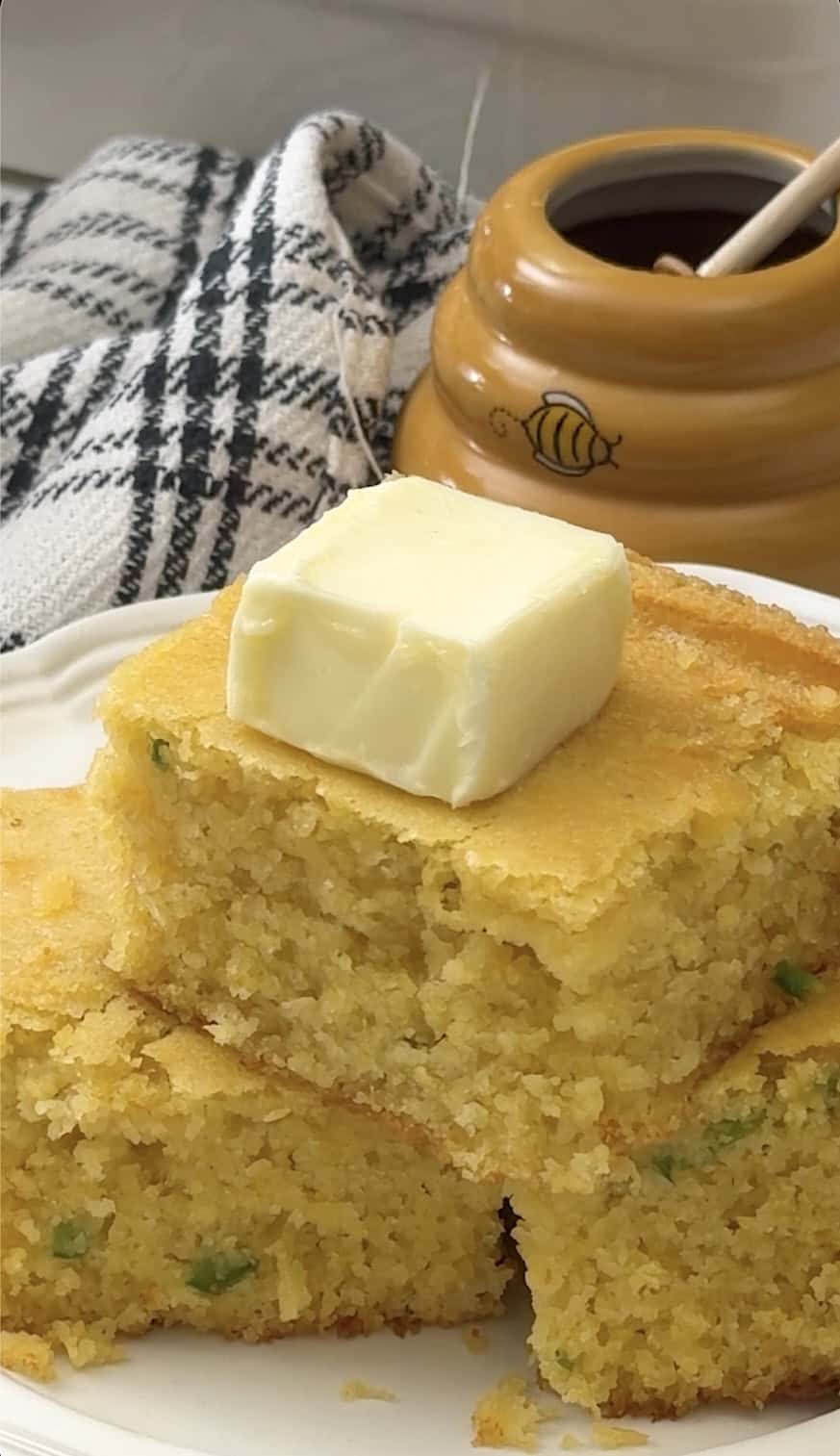 Topping a stack of skillet cornbread with butter for a great bread side.