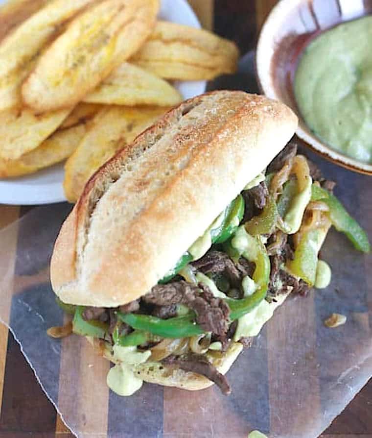 A steak and pepper sandwich with fried plantains and dressing.