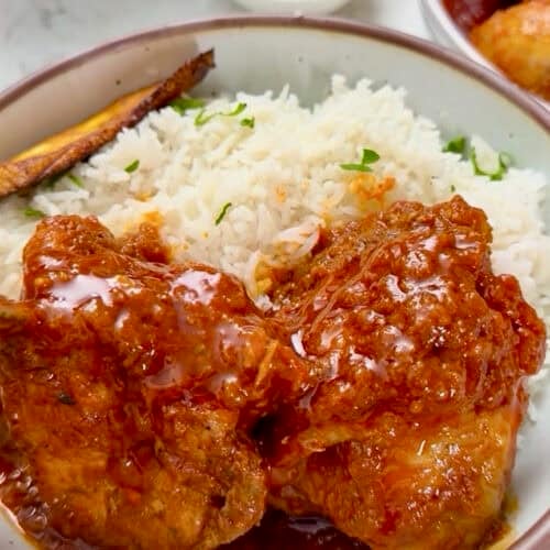 An African chicken dinner with a delicious tomato-based sauce, fried plantains, and coconut rice.