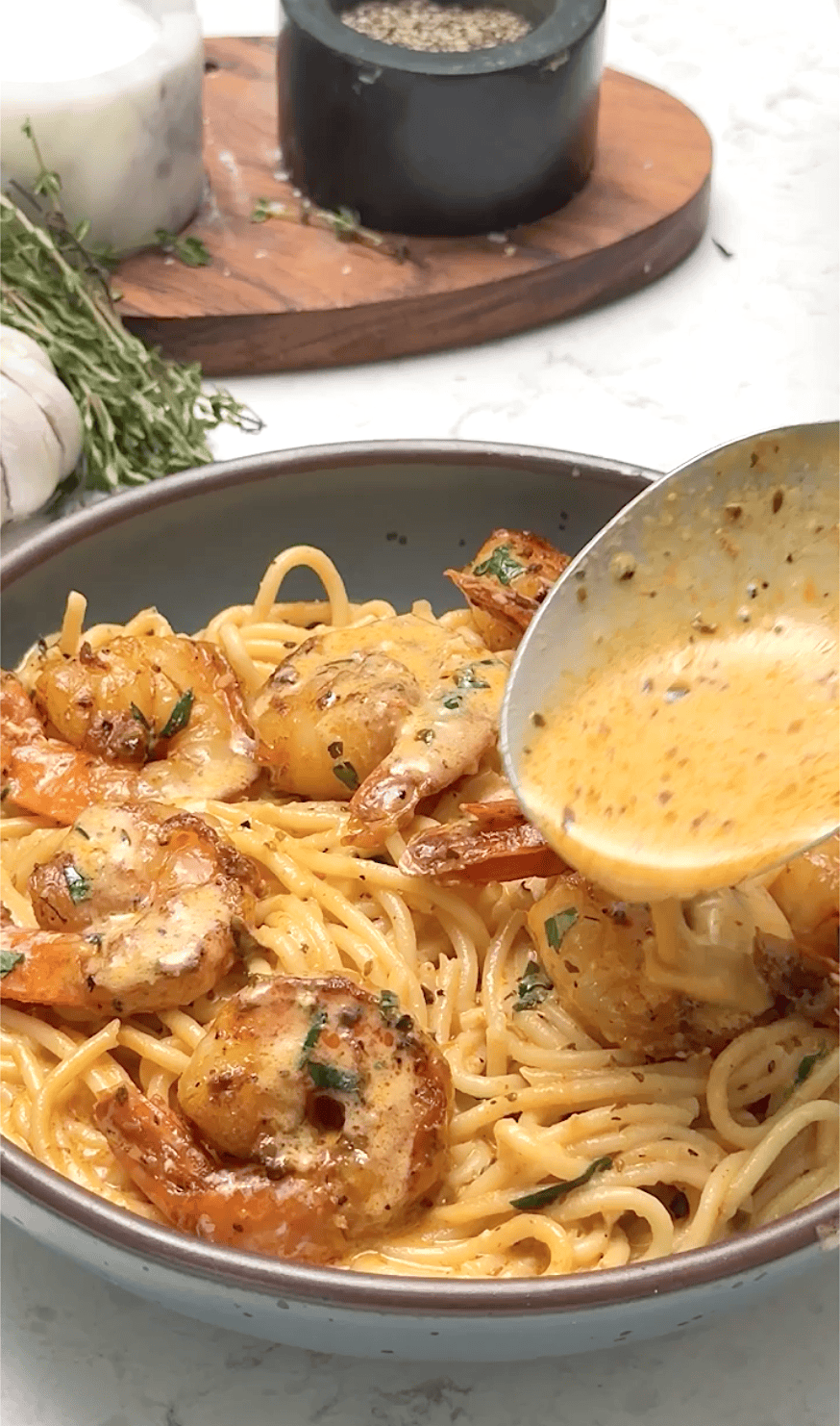 Adding more cream sauce to the bowl of shrimp and pasta.