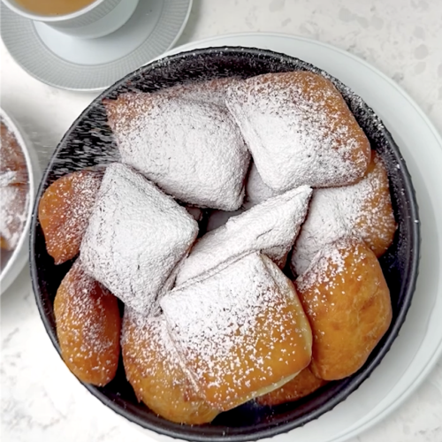Dusting hot New Orleans beignets with powdered sugar. Cafe au lait is ready and waiting.