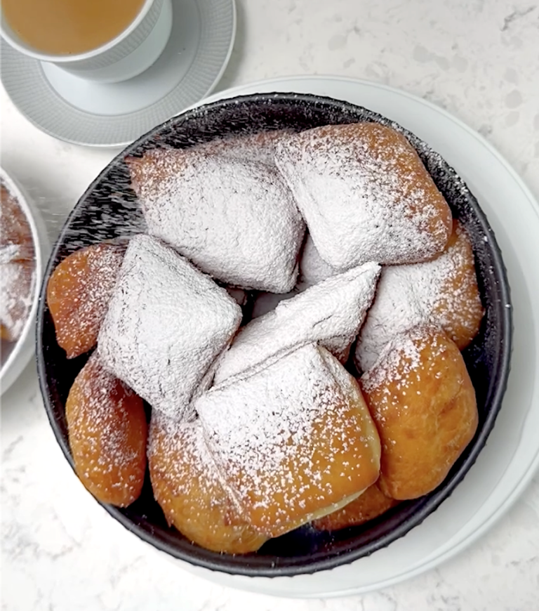 Dusting hot New Orleans beignets with powdered sugar. Cafe au lait is ready and waiting.