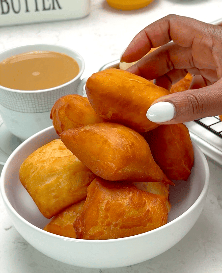 Piling up freshly fried beignets with cafe au lait in the background.