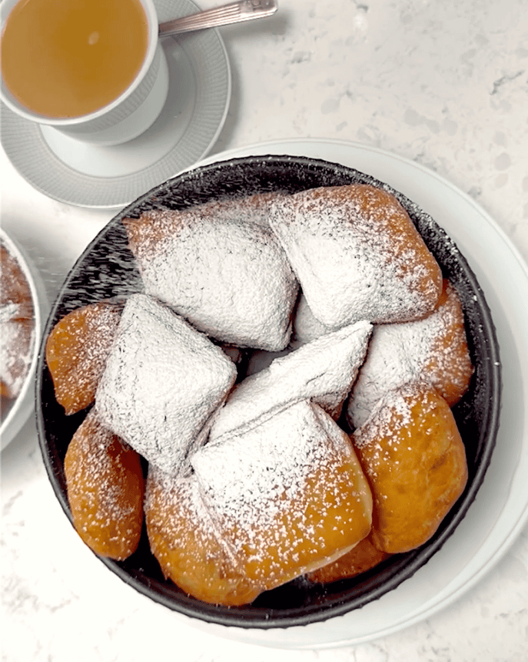 Dusting hot New Orleans beignets with powdered sugar. Cafe au lait is ready and waiting.