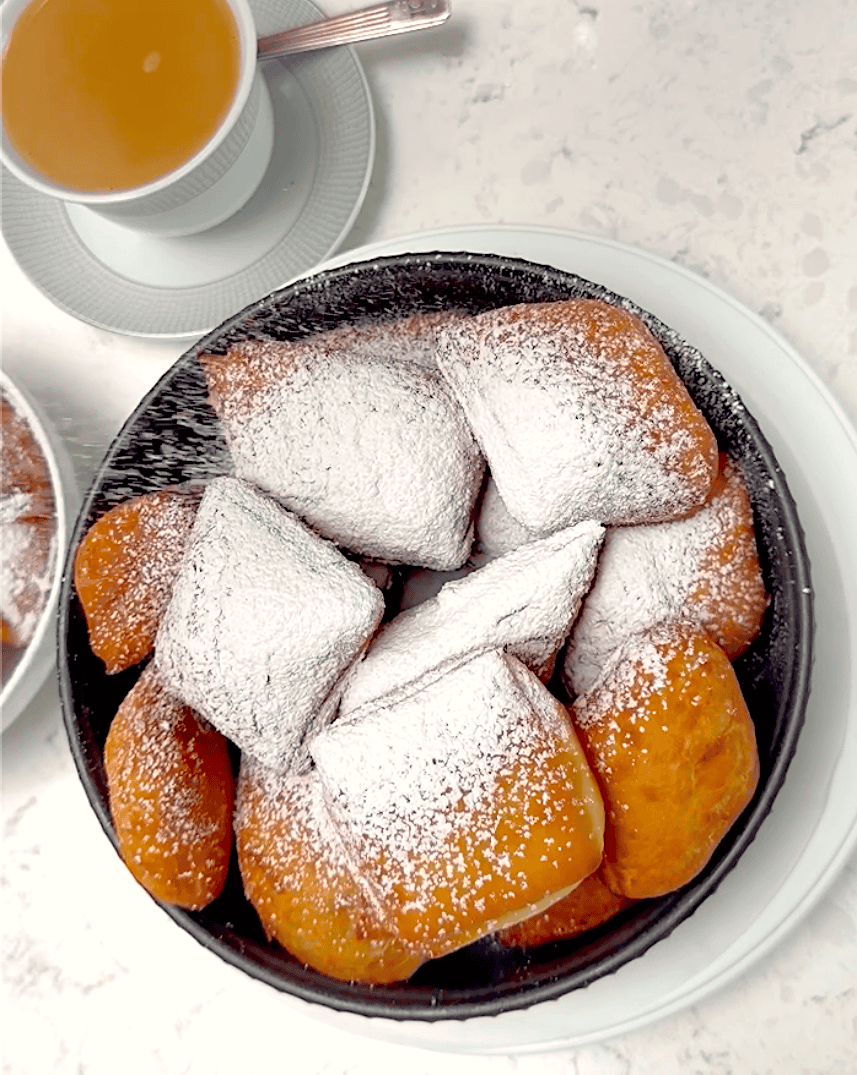Dusting hot New Orleans beignets with powdered sugar. Cafe au lait is ready and waiting.