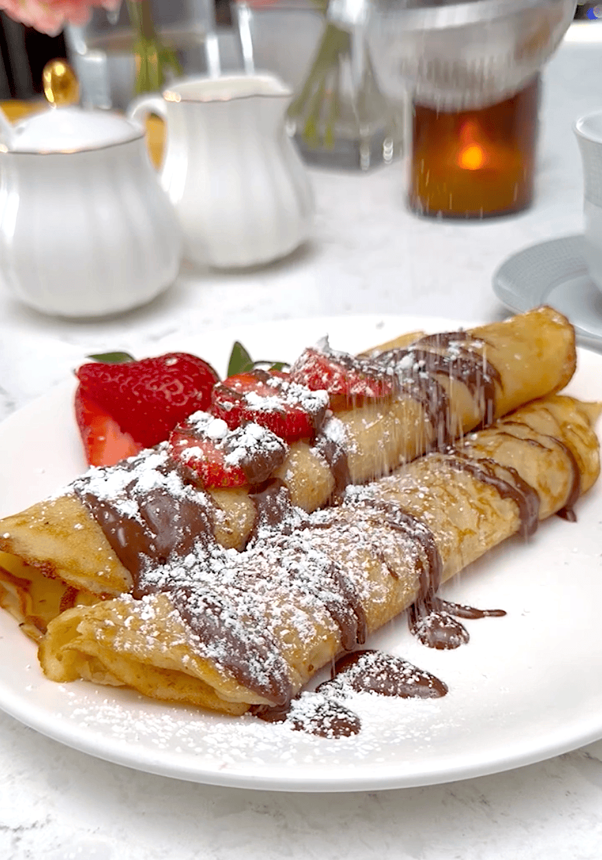 Plantain pancakes drizzled with chocolate sauce, powdered sugar, and sliced strawberries.