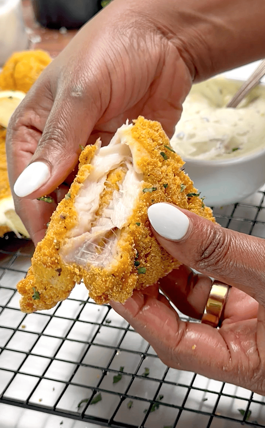 Breaking open a freshly fried fish fillet to reveal the flaky white interior.