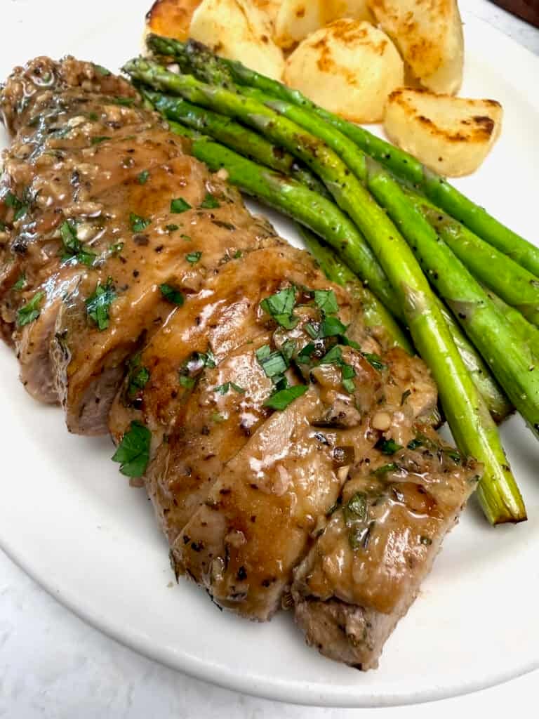 A marinated pork tenderloin roast, sliced and ready to enjoy with asparagus and roasted potatoes.