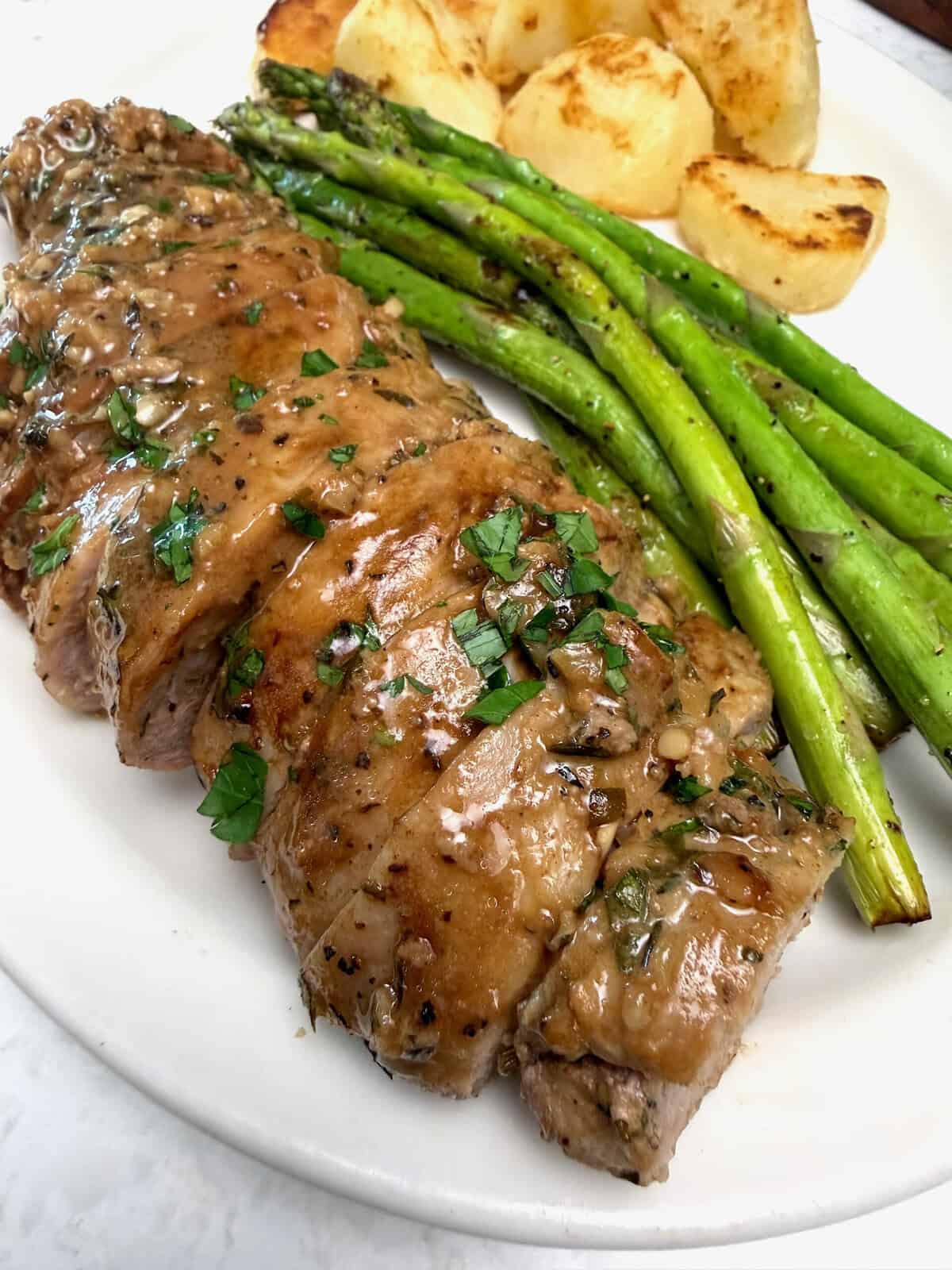 A marinated pork tenderloin roast, sliced and ready to enjoy with asparagus and roasted potatoes.