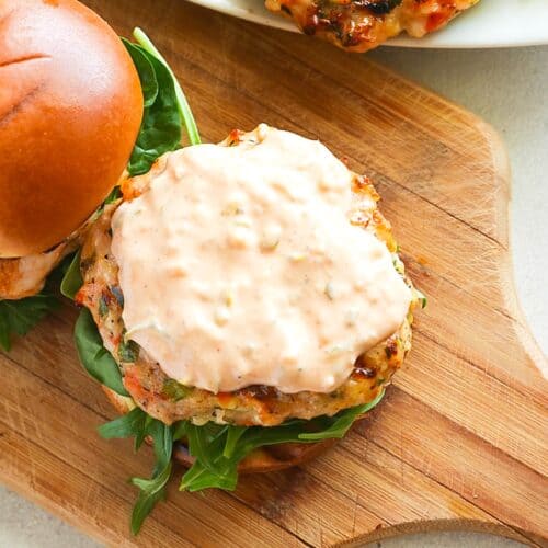 Topping a salmon burger with a homemade all-purpose sauce.