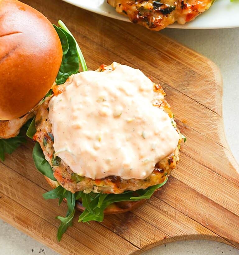 Topping a salmon burger with a homemade all-purpose sauce.