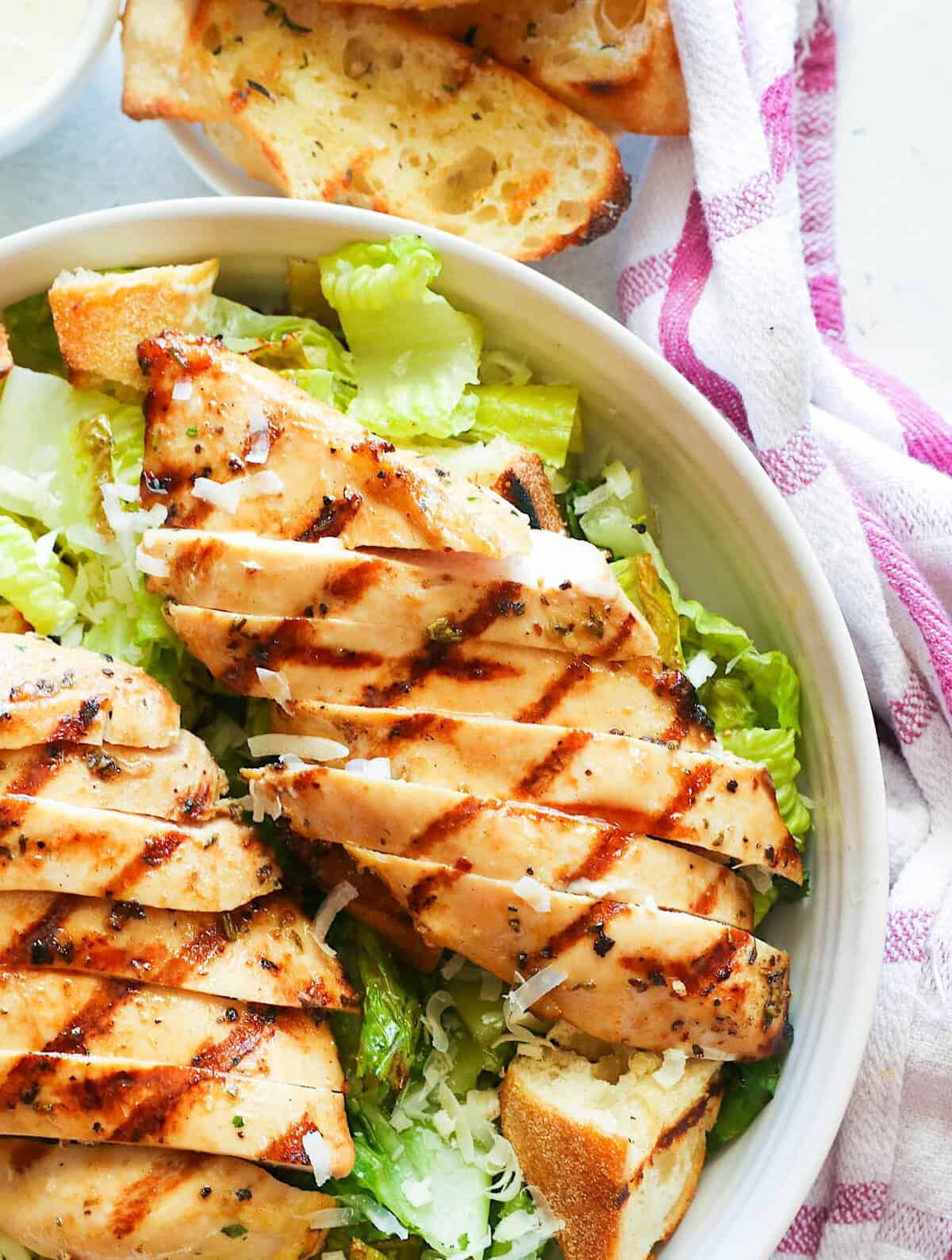 A freshly assembled Caesar salad topped with grilled chicken and accompanied by toasted French bread or croutons. 