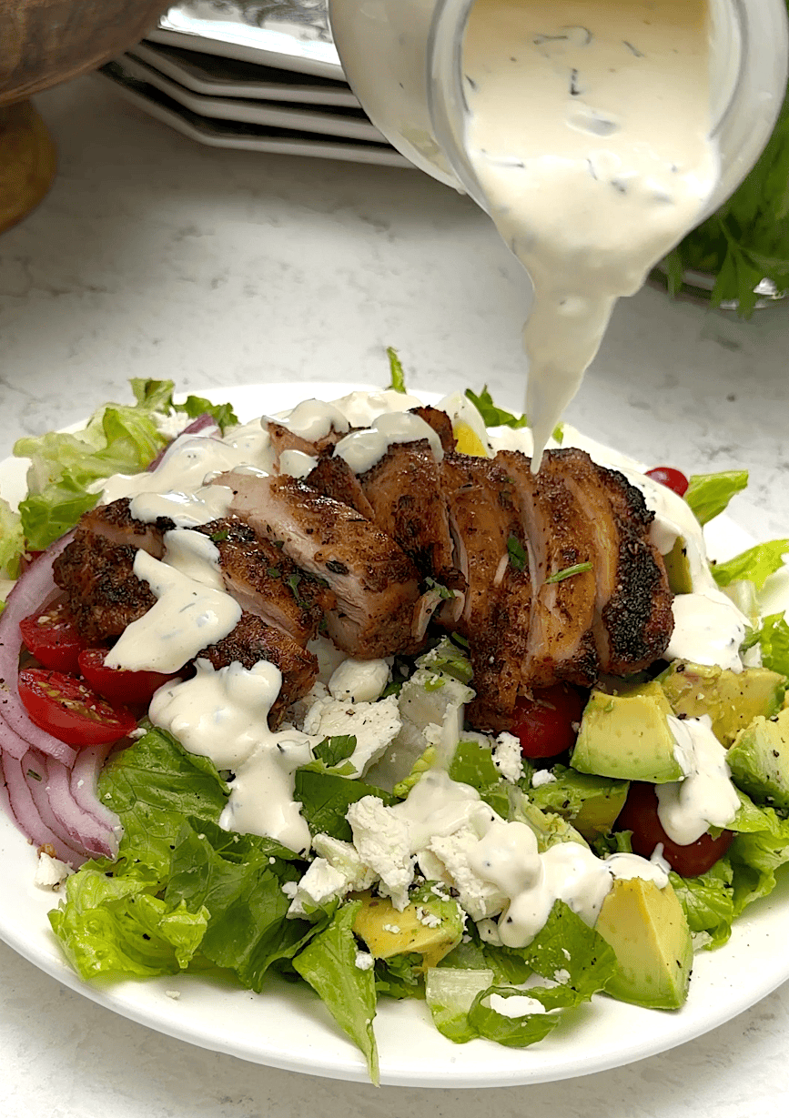 Drizzling homemade salad dressing over a refreshing salad with chicken and avocado.
