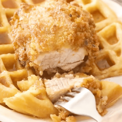 Slicing into fried chicken topping a waffle, showing off the juicy breast meat.
