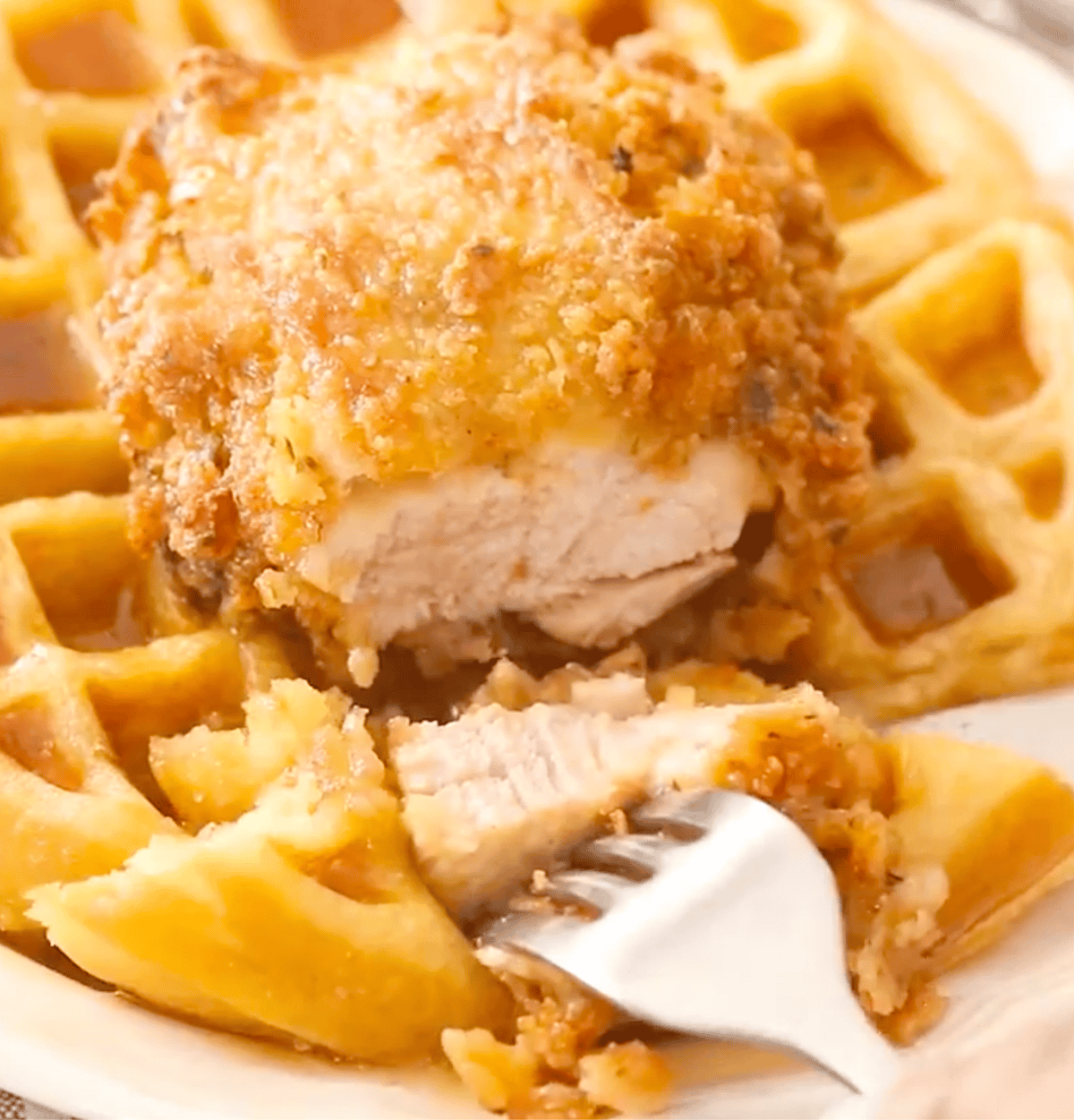 Slicing into fried chicken topping a waffle, showing off the juicy breast meat.