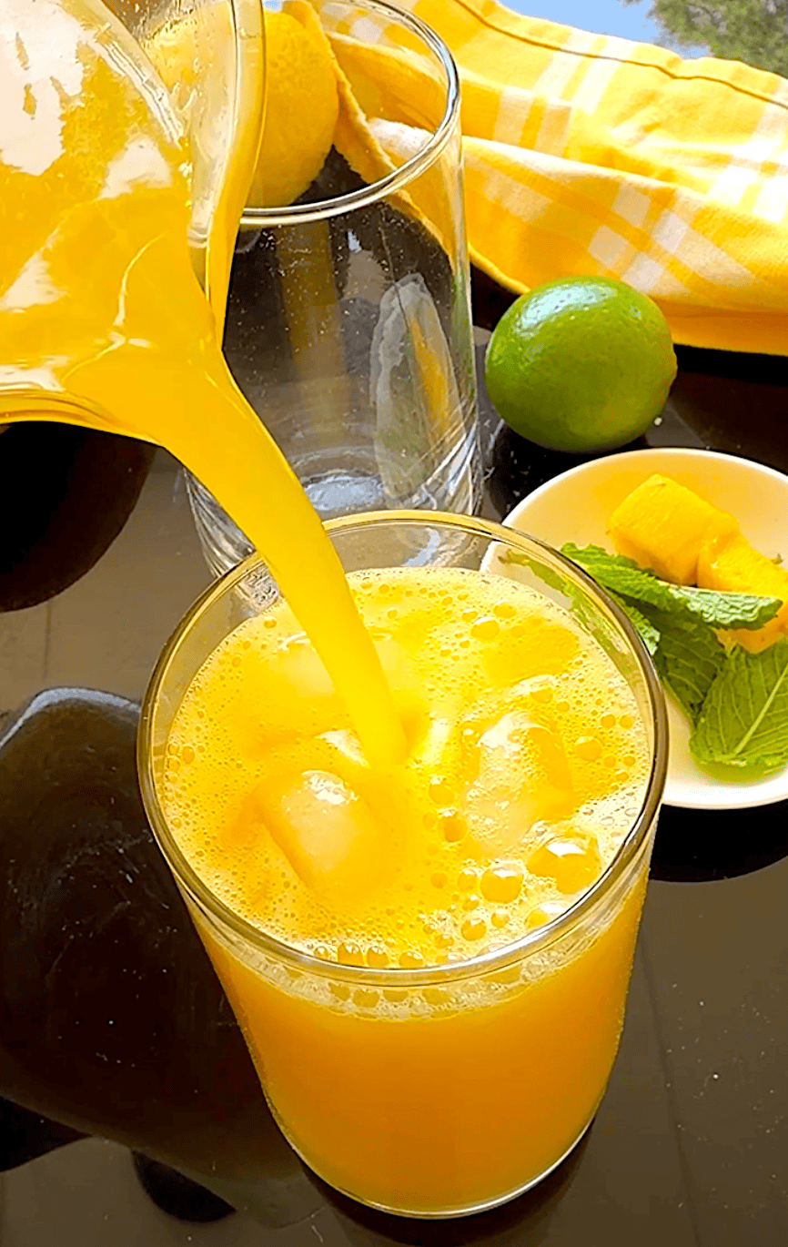 Pouring a chilled glass of mango lemonade over ice.