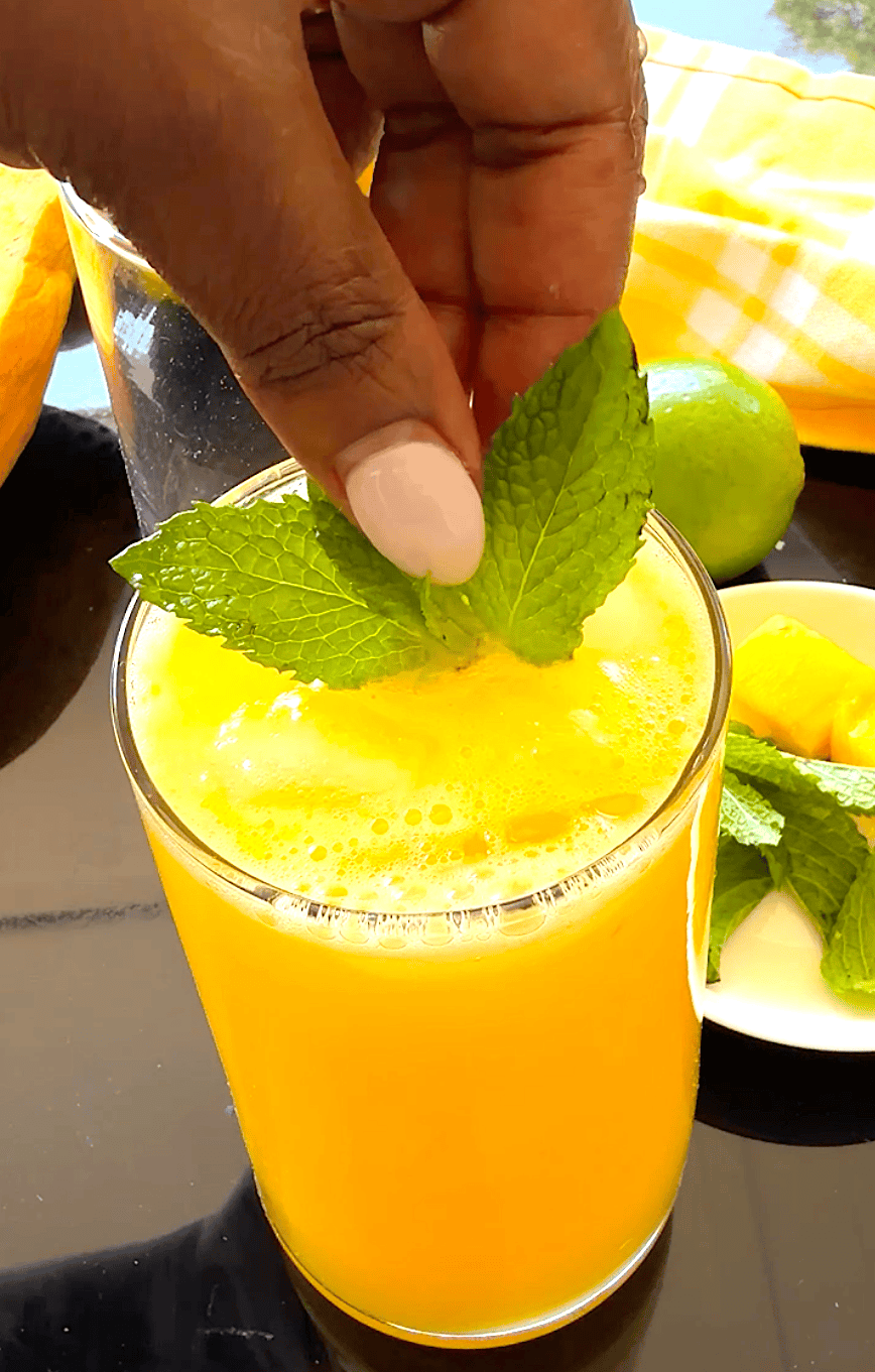 Garnishing an ice-cold glass of mango lemonade with mint leaves.