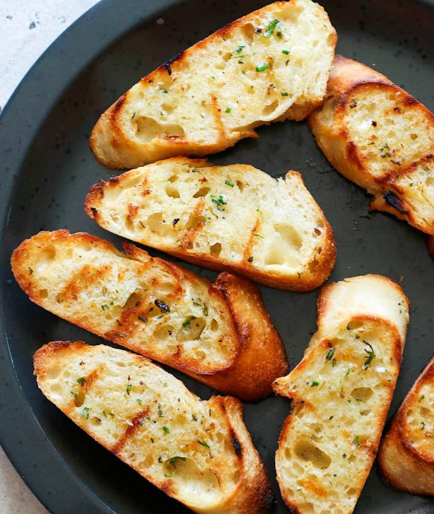 Freshly grilled bread spread with herbed butter waiting to accompany steak and potatoes with a refreshing tossed salad.